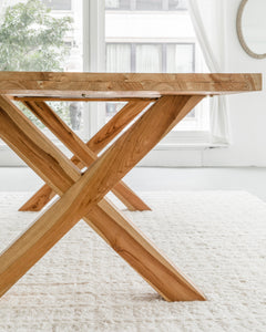 side profile of an elegant yet rustic teak dining table in solid wood with cross legs, including views of the natural wood grain
