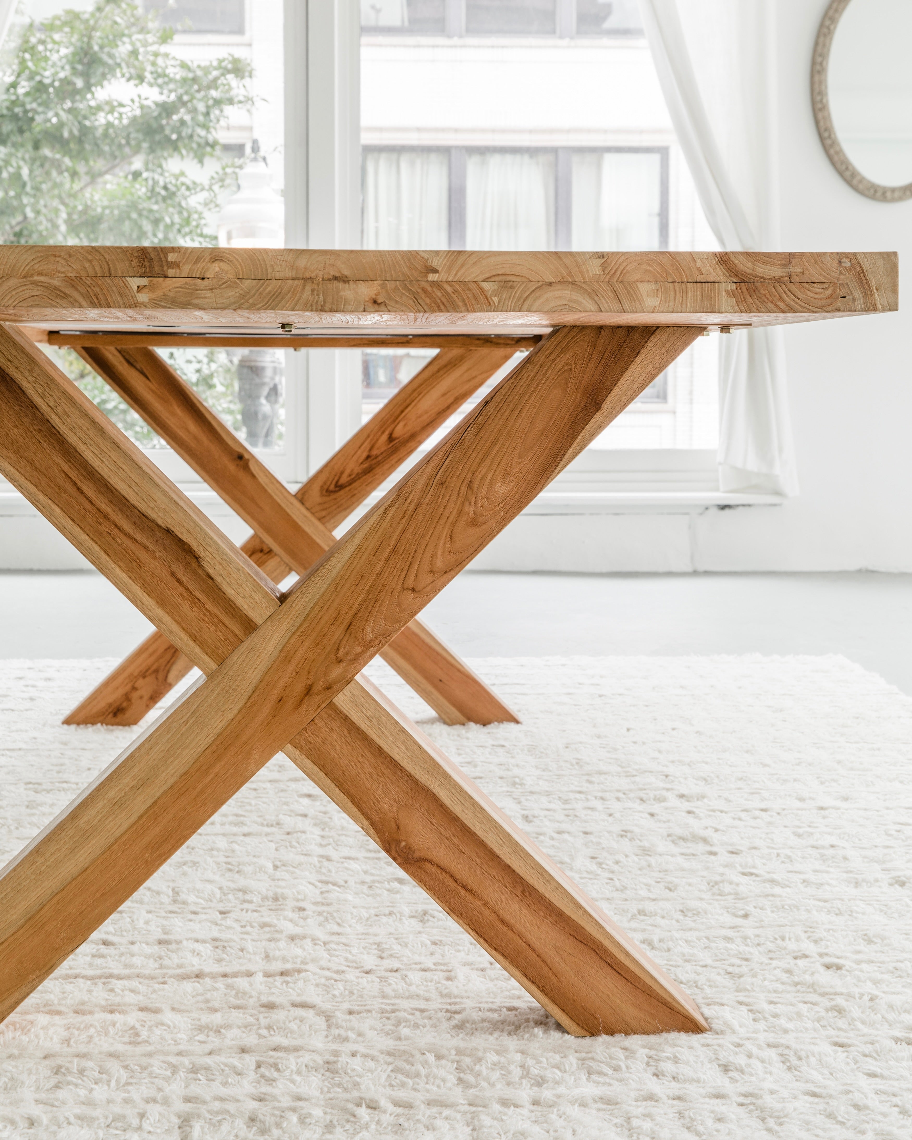 side profile of an elegant yet rustic teak dining table in solid wood with cross legs, including views of the natural wood grain