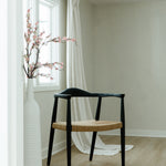 peak through the door view of a matte black and jute rope woven seat dining chair in a bright room