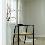 peak through the door view of a matte black and jute rope woven seat dining chair in a bright room