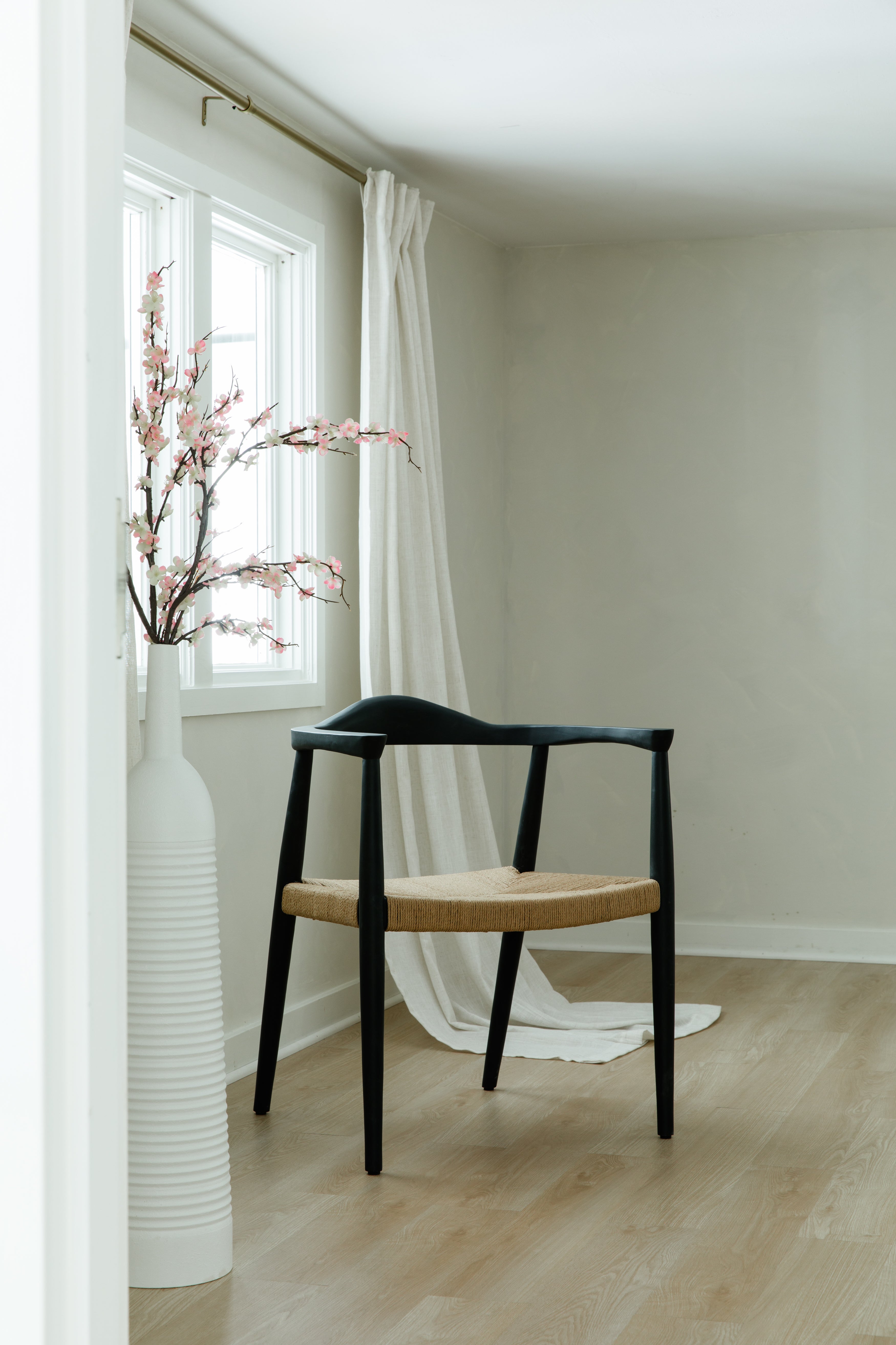 peak through the door view of a matte black and jute rope woven seat dining chair in a bright room