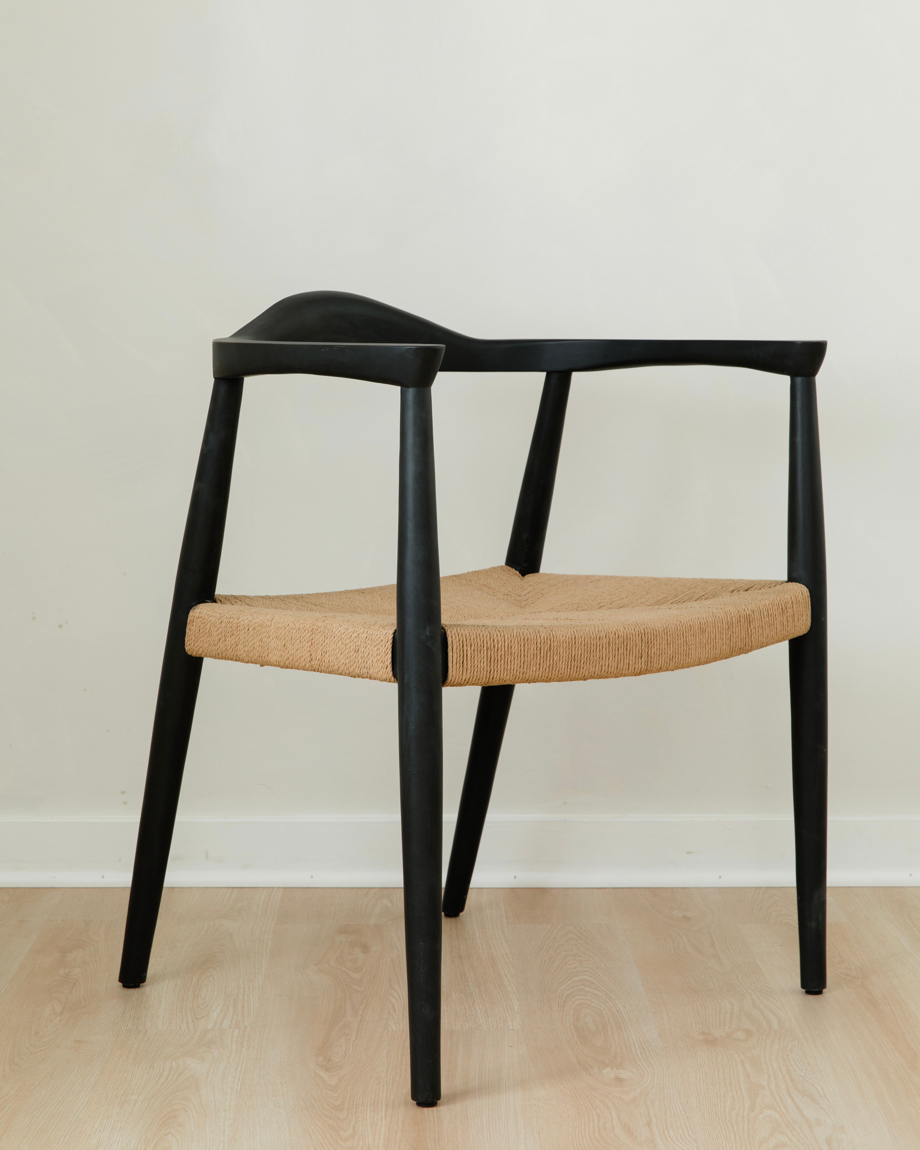 angular view of a minimal matte black dining room chair with a curved back and a jute rope woven seat