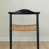 back view of a sustainable matte black dining room chair with a curved back and a jute rope woven seat