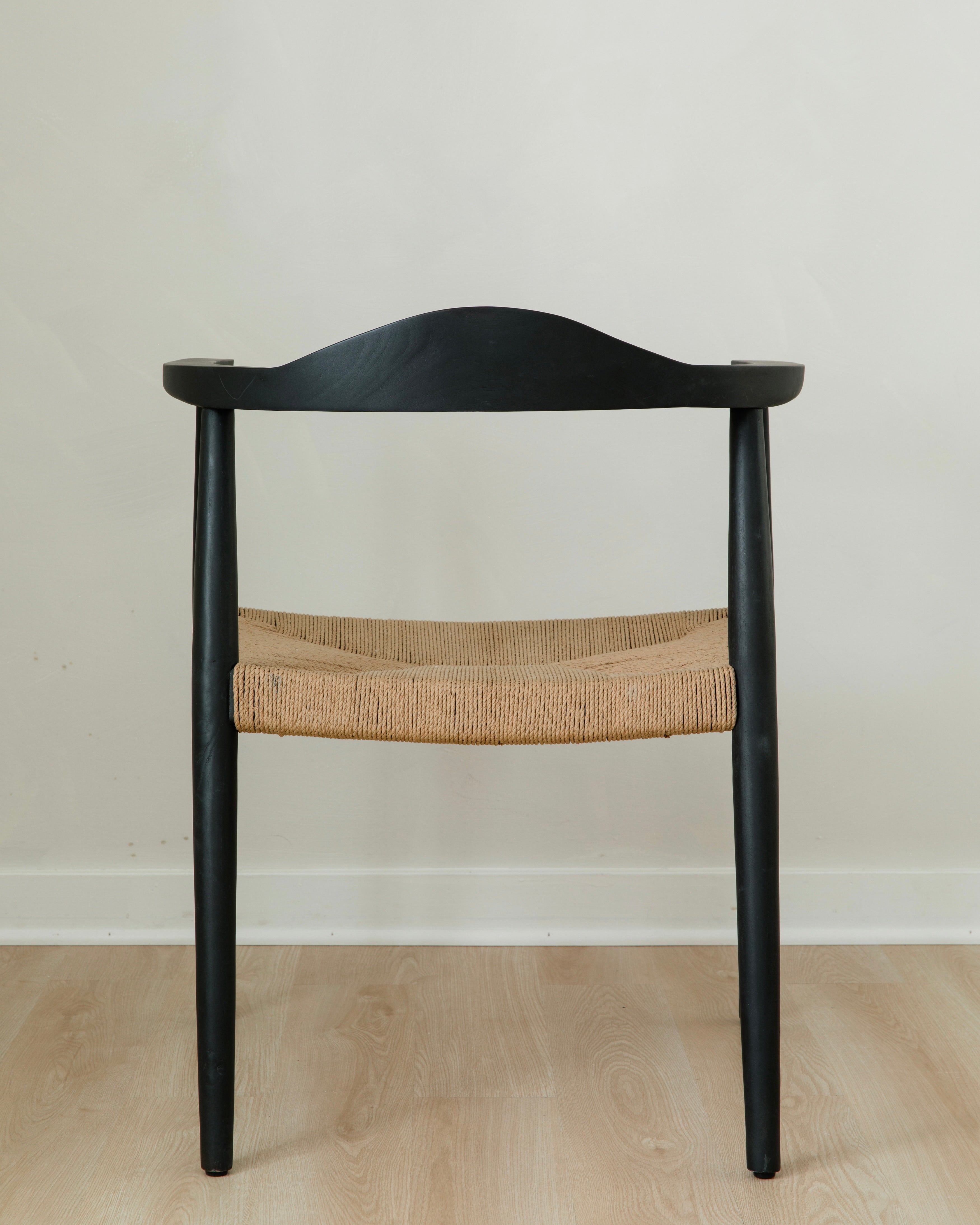 back view of a sustainable matte black dining room chair with a curved back and a jute rope woven seat