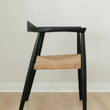 side view of a sustainable matte black dining room chair with a curved back and a jute rope woven seat