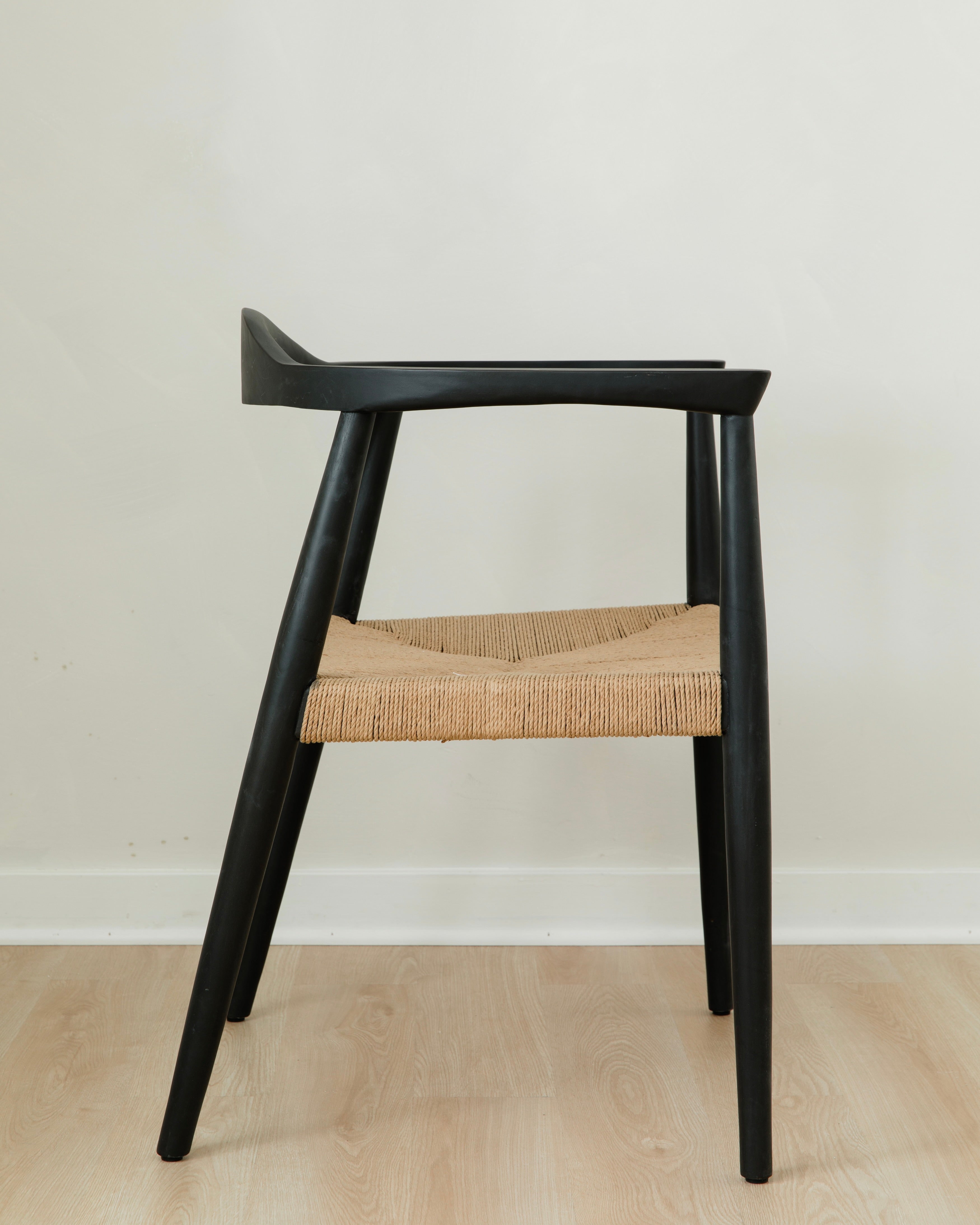 side view of a sustainable matte black dining room chair with a curved back and a jute rope woven seat