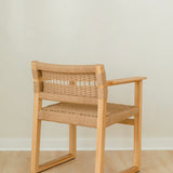 angular back view of a natural wooden dining chair with arms and a woven jute rope seat and back