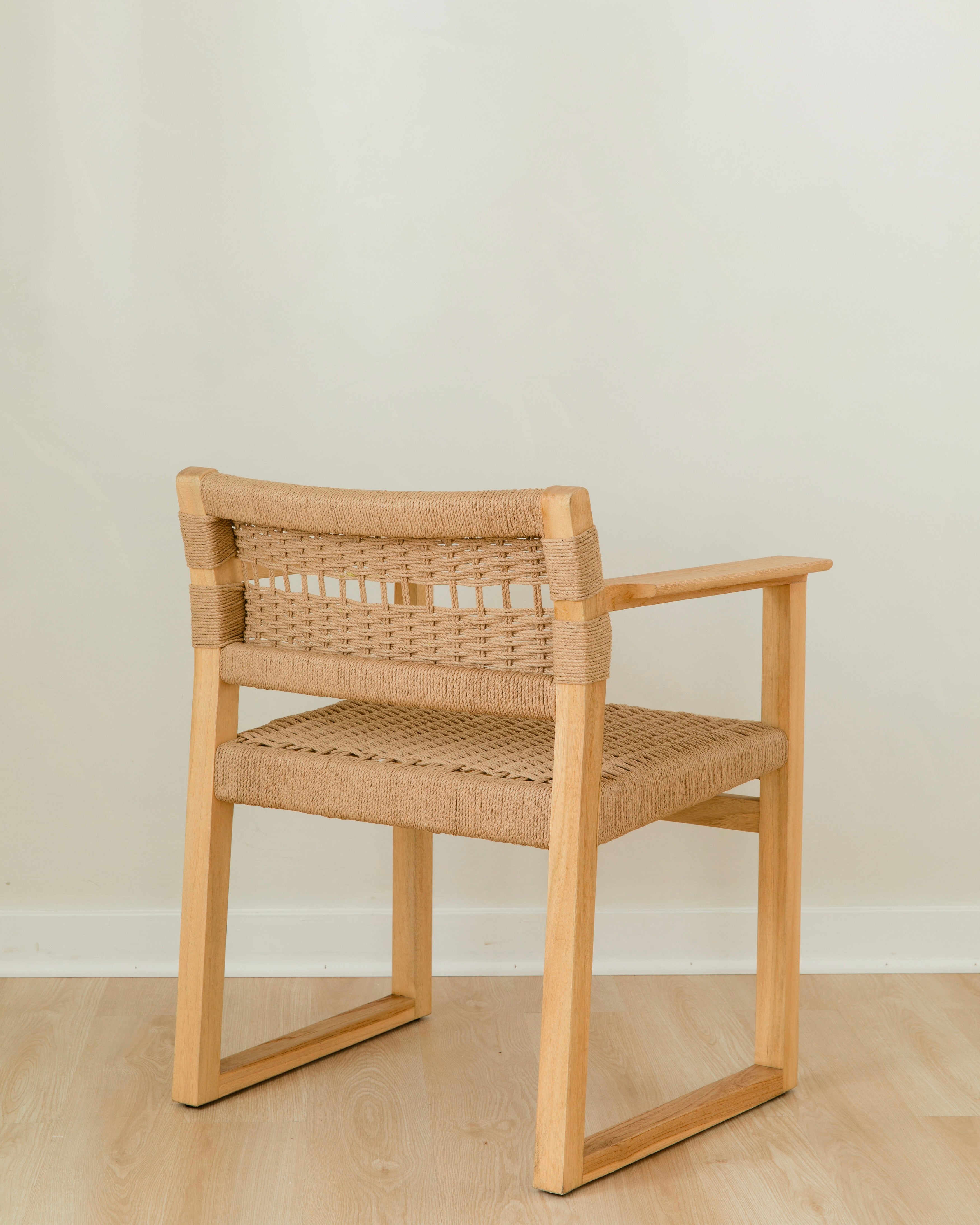 angular back view of a natural wooden dining chair with arms and a woven jute rope seat and back