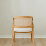 back view of curved and caned accent chair in a natural solid teak wood with a white cushion seat