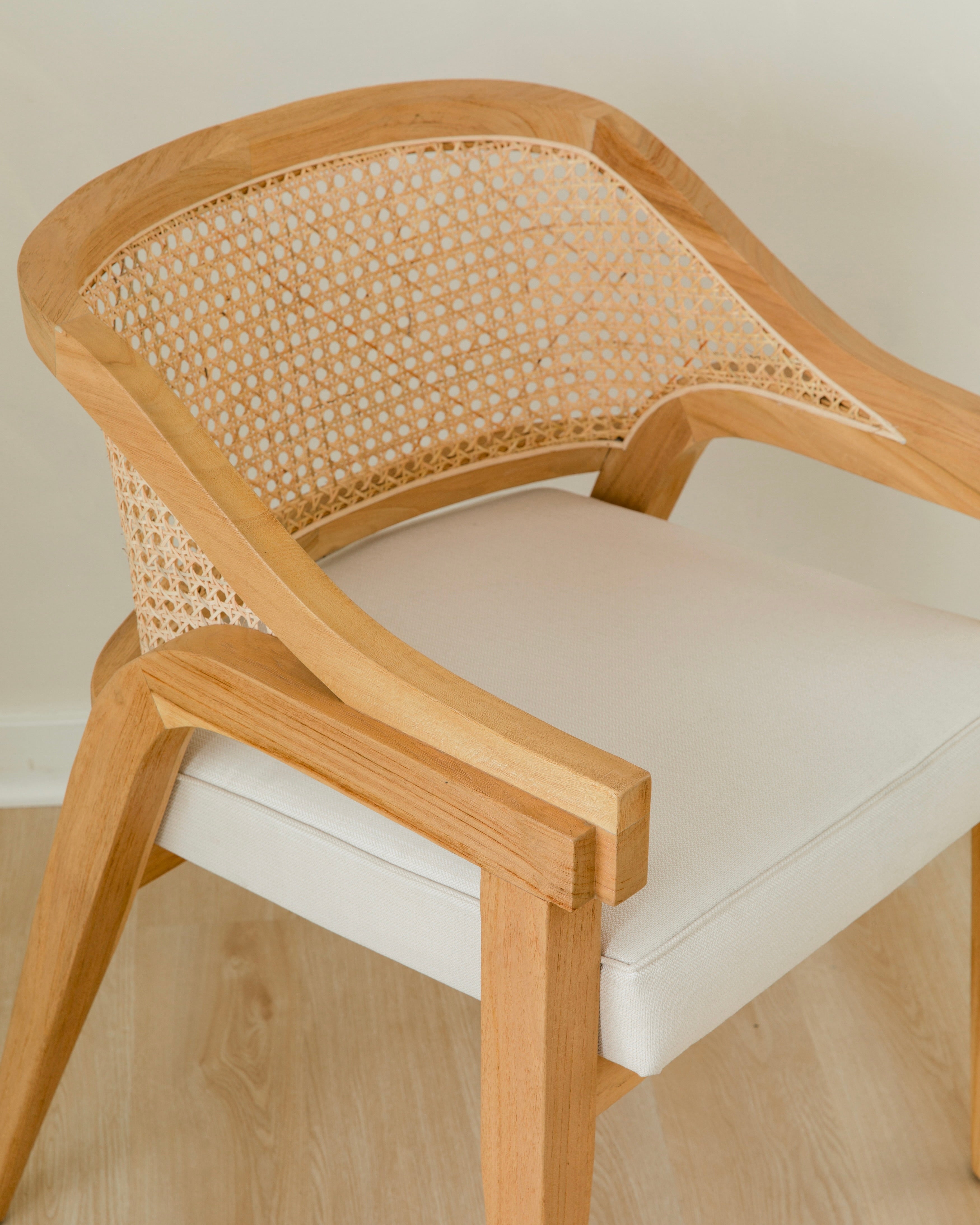 close up view of curved and caned accent chair in a natural solid teak wood with a white cushion seat