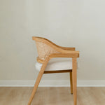side view of curved and caned accent chair in a natural solid teak wood with a white cushion seat