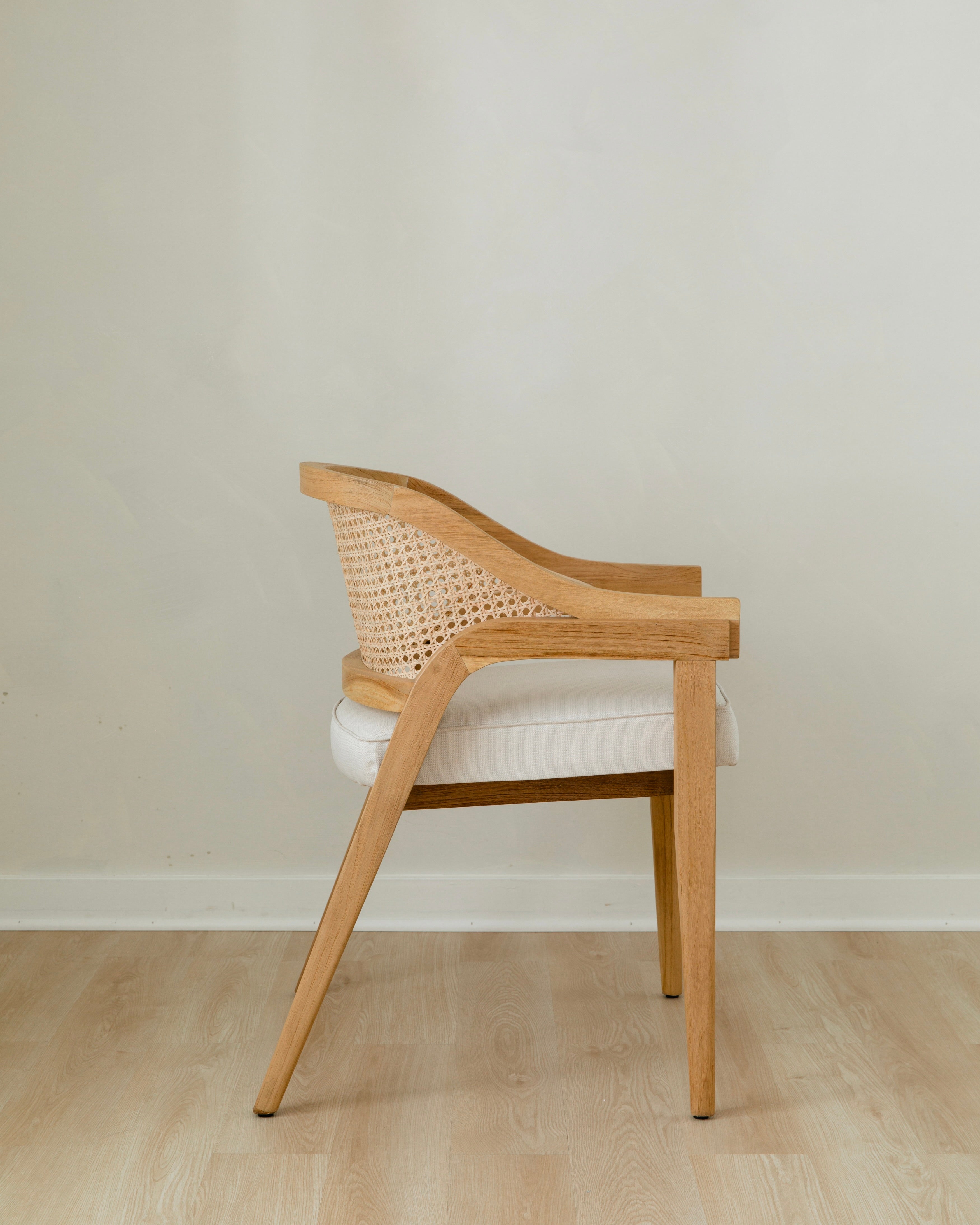 side view of curved and caned accent chair in a natural solid teak wood with a white cushion seat