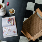 diary view of a checkerboard kitchen floor and a natural wooden and textural arm chair with flowers and decor