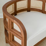close up view of curved and caned accent chair in a club style with a walnut wooden stain finish and white cushion
