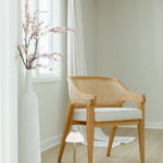 peek through the door of a bright room with a sustainable wooden and caned chair with a white cushion seat