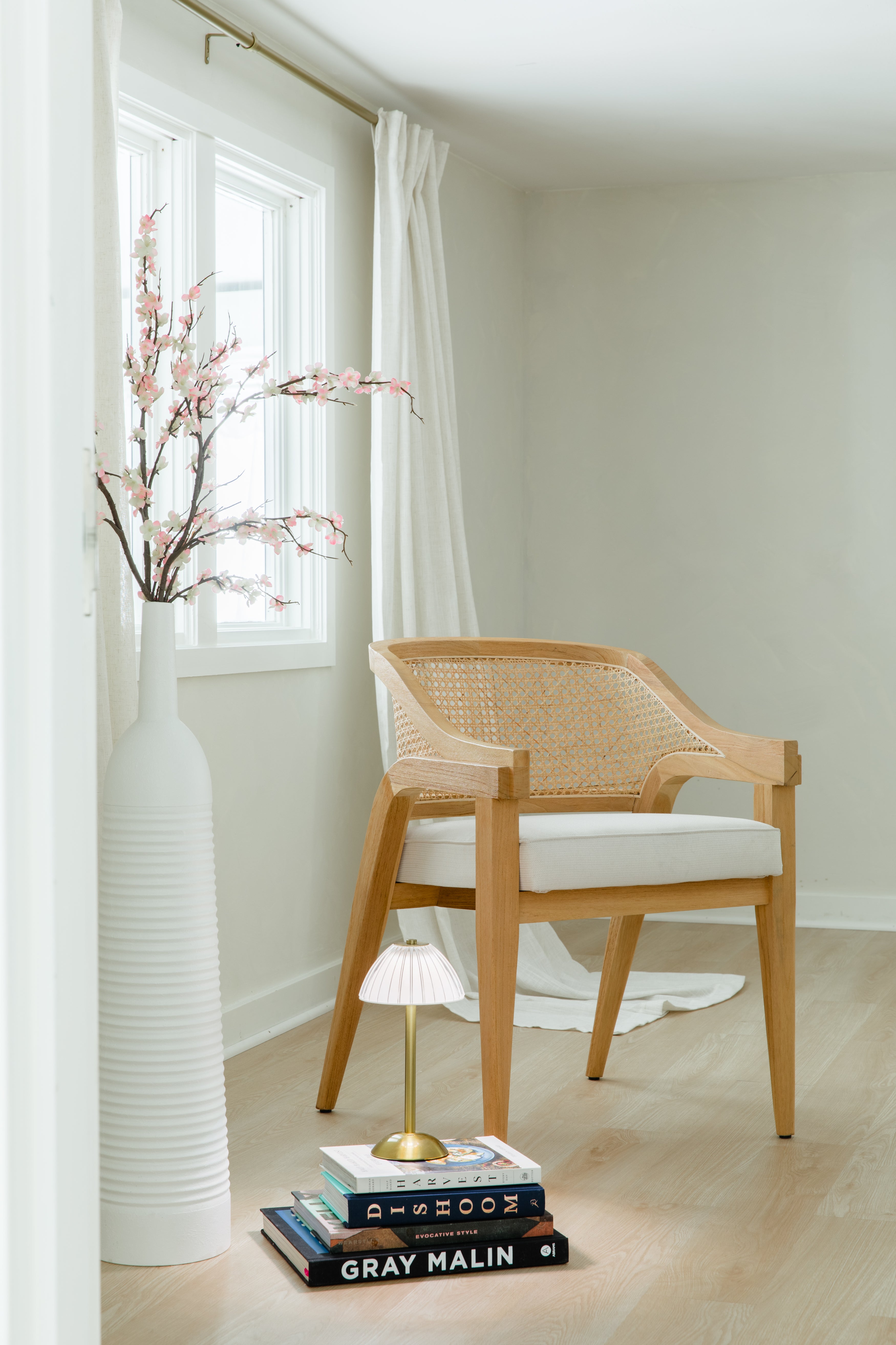 peek through the door of a bright room with a sustainable wooden and caned chair with a white cushion seat