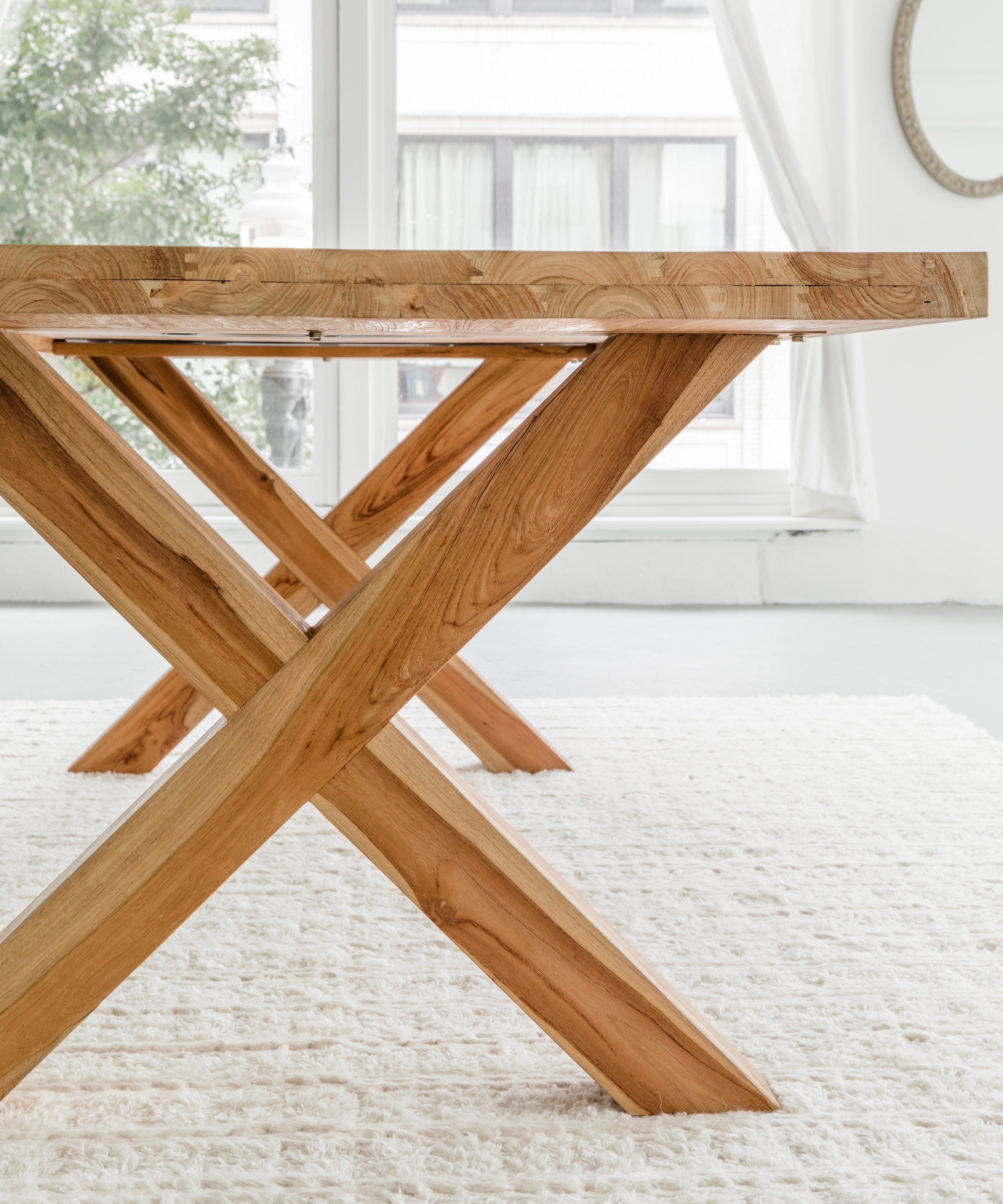 side profile of an elegant yet rustic teak dining table in solid wood with cross legs, including views of the natural wood grain