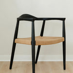 angular view of a minimal matte black dining room chair with a curved back and a jute rope woven seat