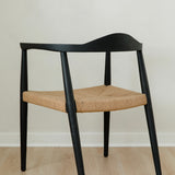 angular back view of a modern matte black dining room chair with a curved back and a jute rope woven seat