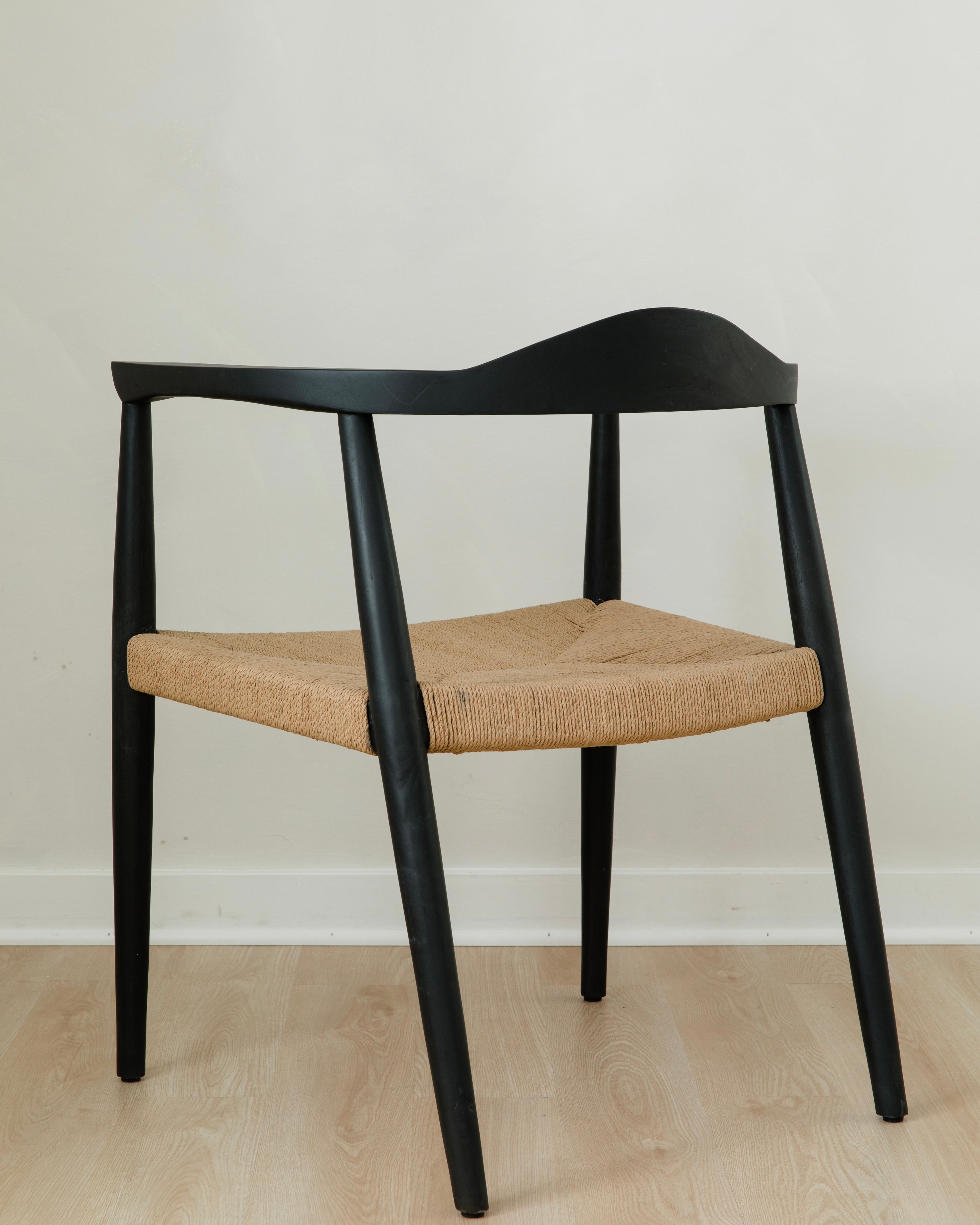 angular back view of a modern matte black dining room chair with a curved back and a jute rope woven seat