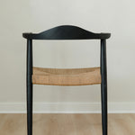 back view of a sustainable matte black dining room chair with a curved back and a jute rope woven seat