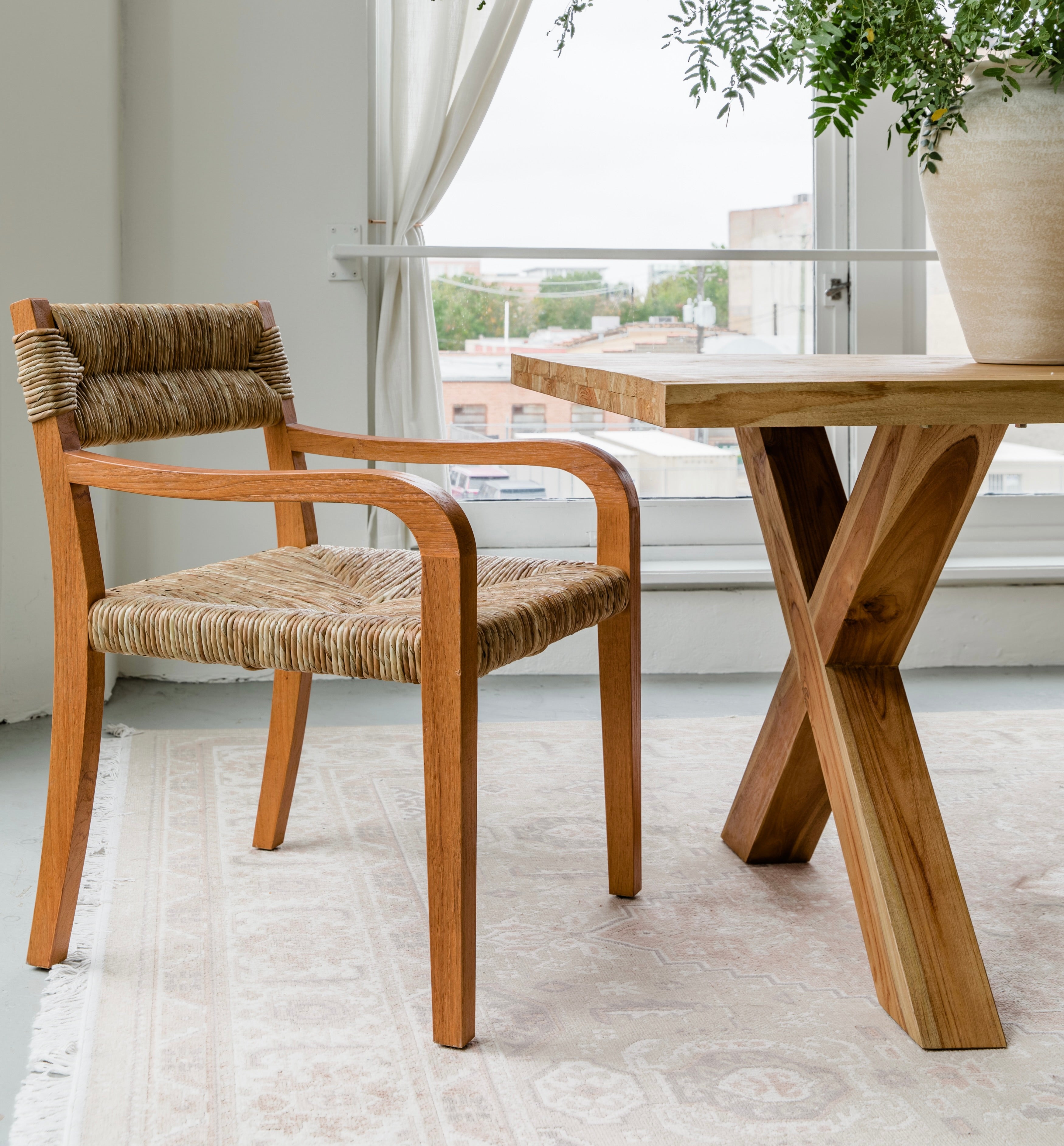 Dining room nook with a seagrass arm dining chair and a cross leg teak wooden table with a natural finish