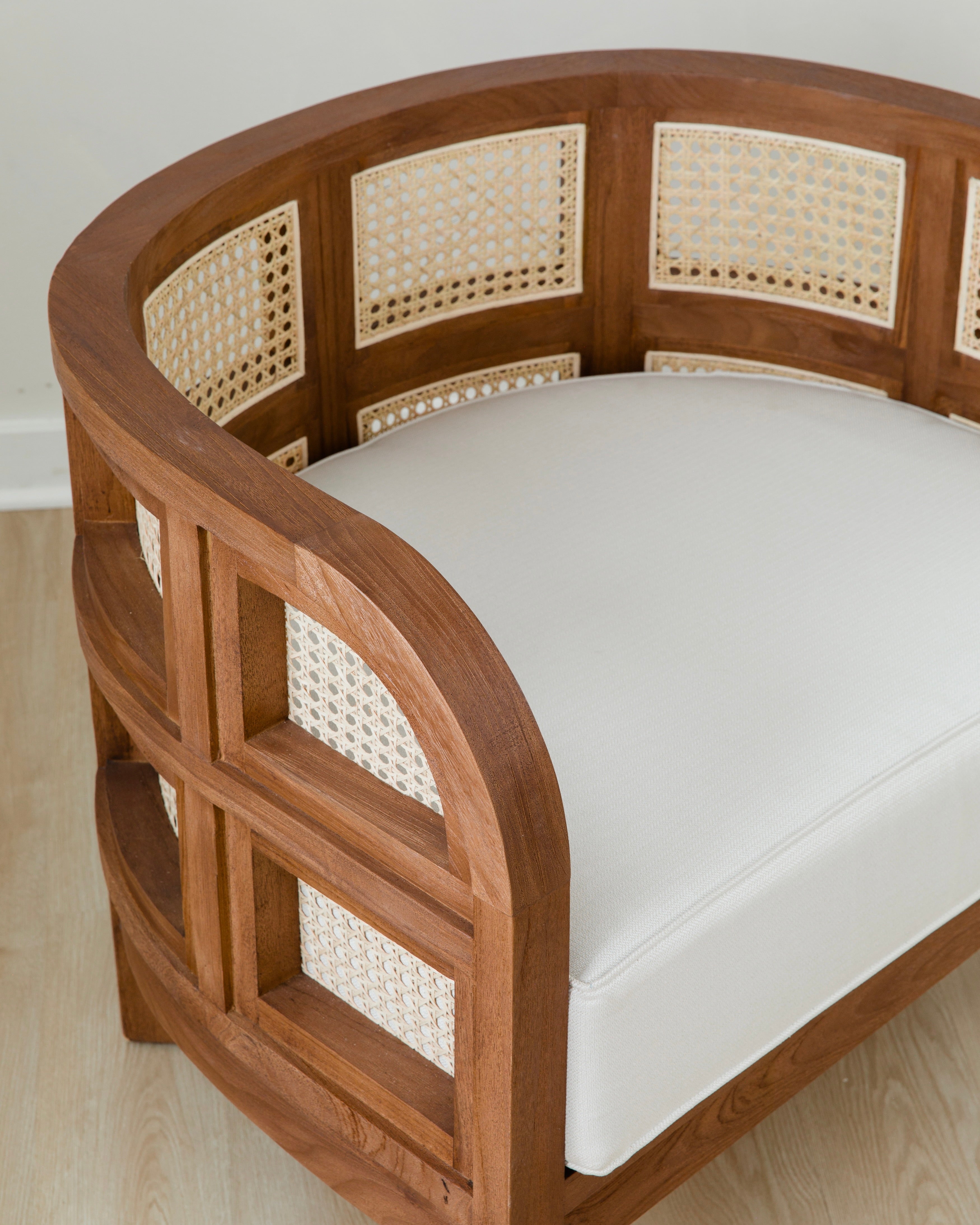 close up view of curved and caned accent chair in a club style with a walnut wooden stain finish and white cushion