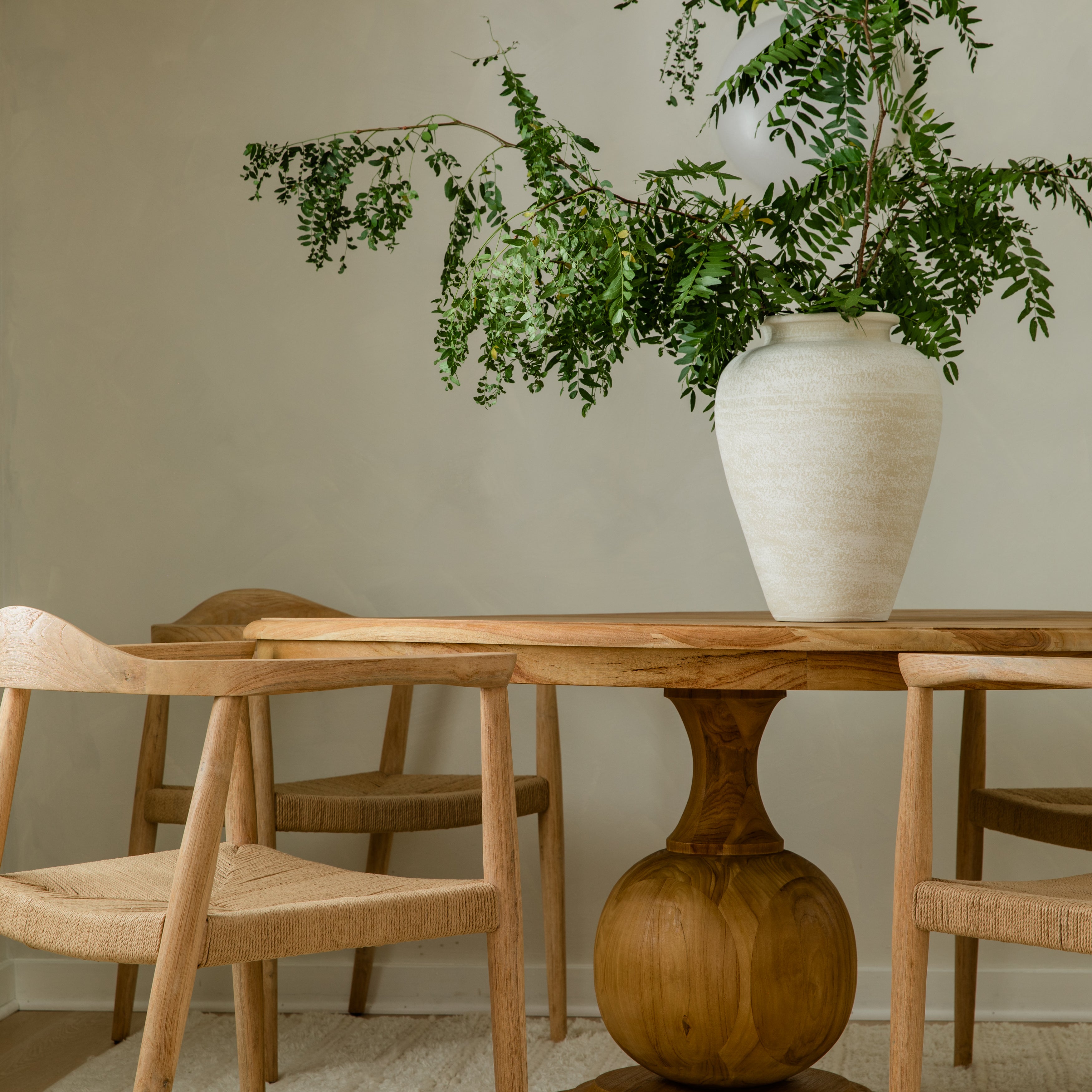 close up view of a dining room highlighting the round ball pedestal base of a wooden dining table surrounded by natural wooden chairs