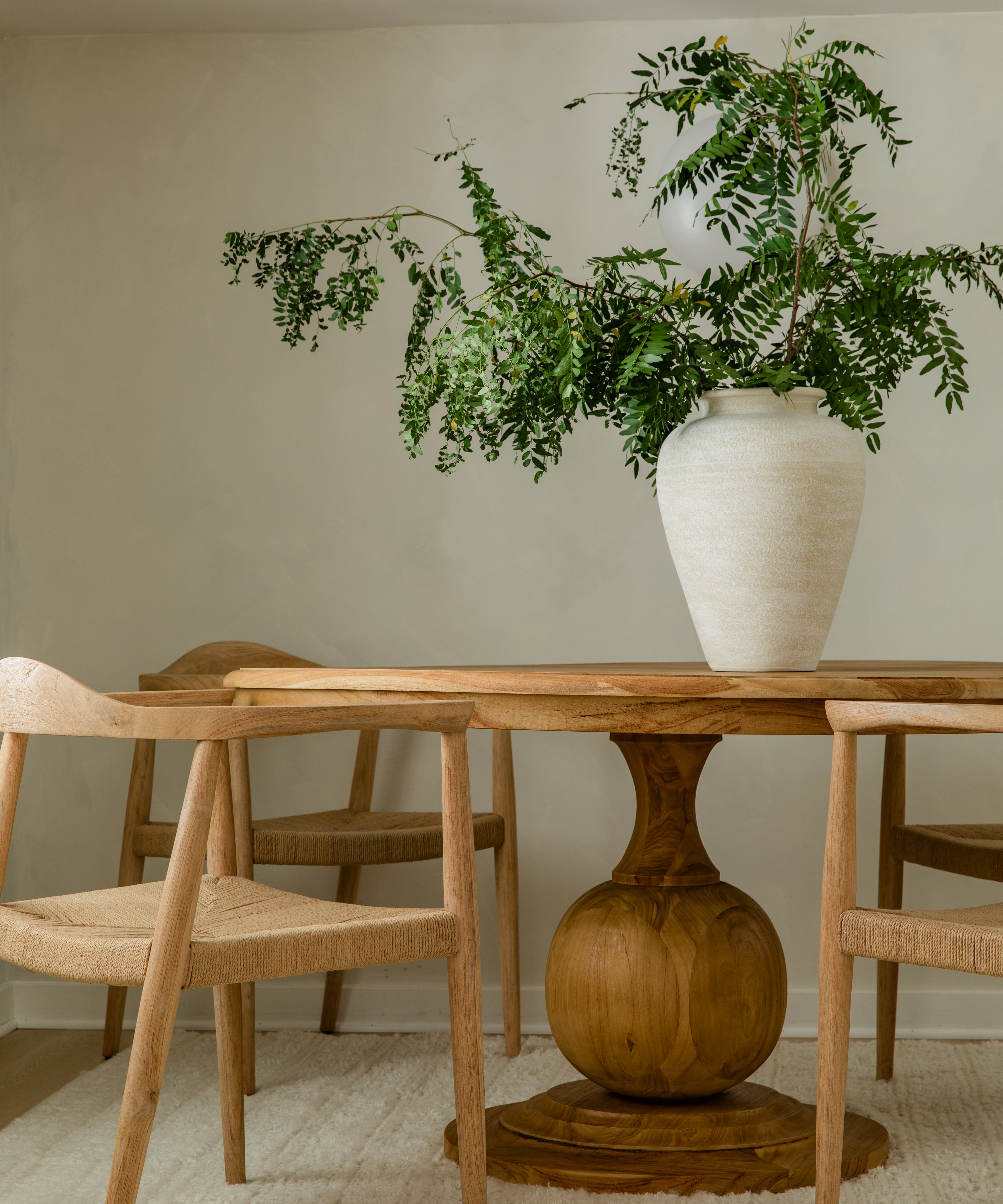 close up view of a dining room highlighting the round ball pedestal base of a wooden dining table surrounded by natural wooden chairs